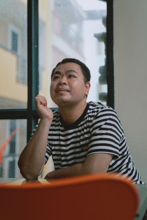 Free A man sitting indoors, looking contemplative near a window in Ho Chi Minh City. Stock Photo