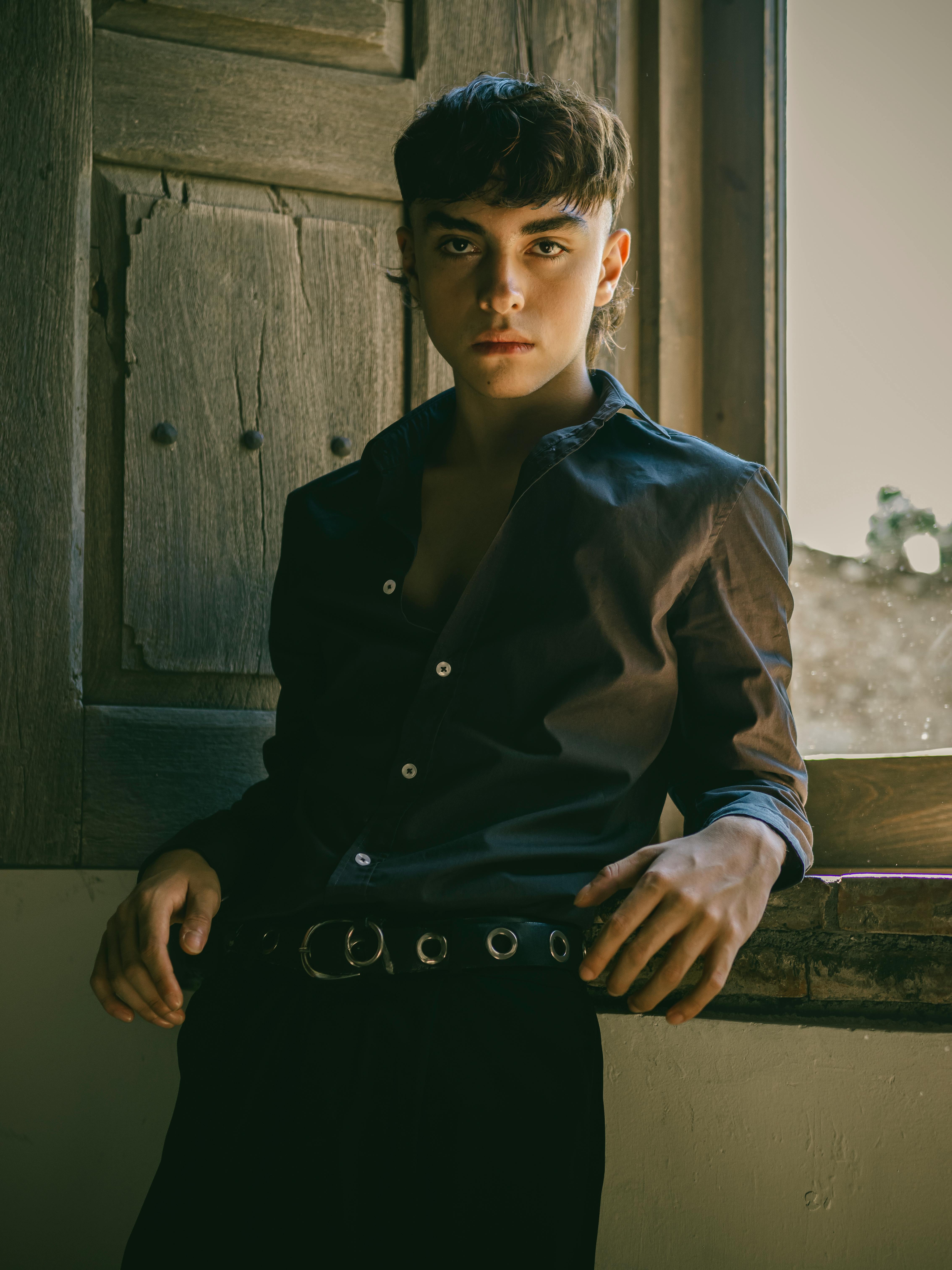 Stylish portrait of a young man standing by a window, showcasing casual fashion.
