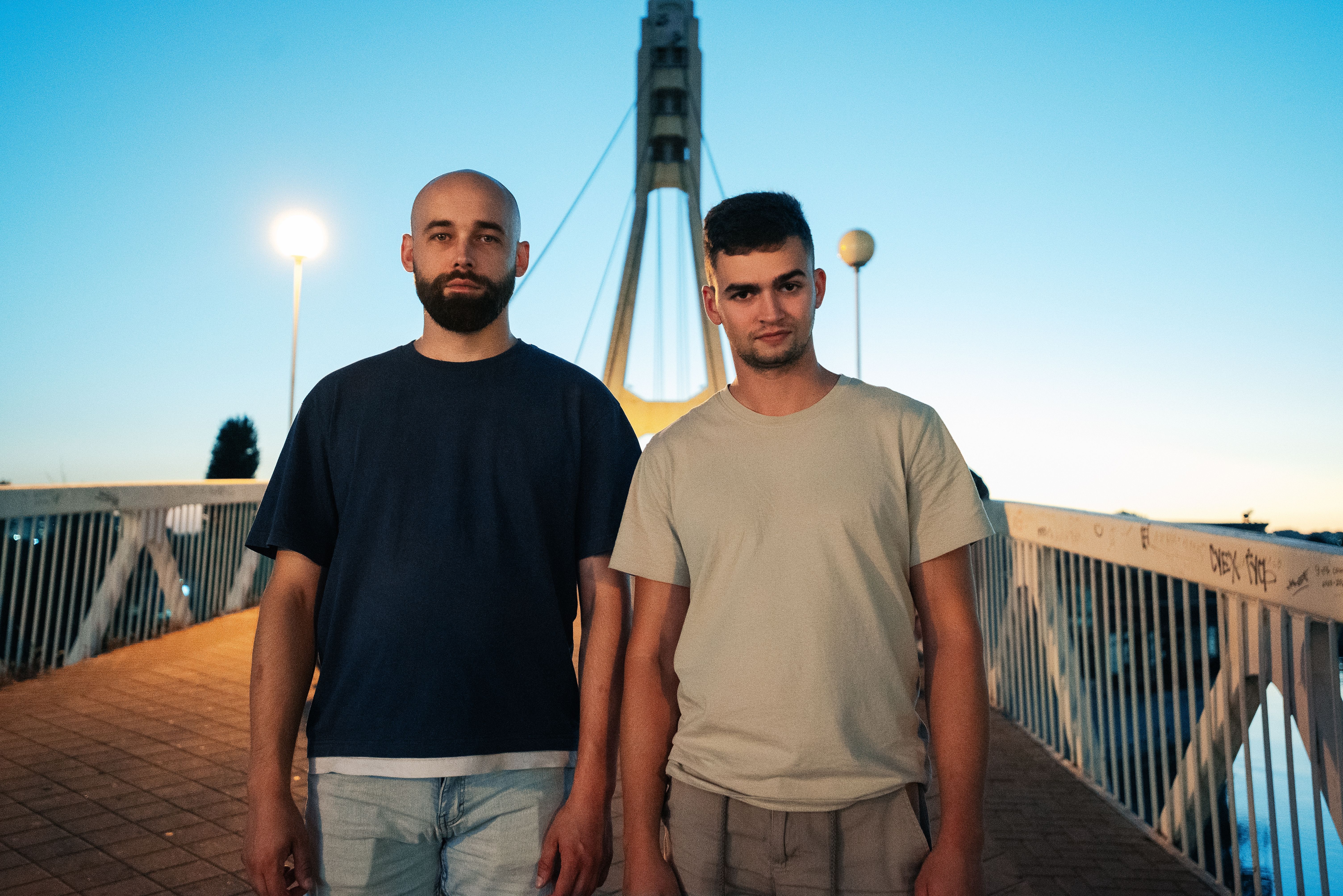 Two men posing casually on a bridge in Russia at sunset, capturing a relaxed mood.