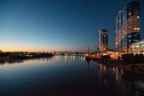 Free A beautiful cityscape at dusk with illuminated buildings and calm river reflections, capturing serene urban life. Stock Photo