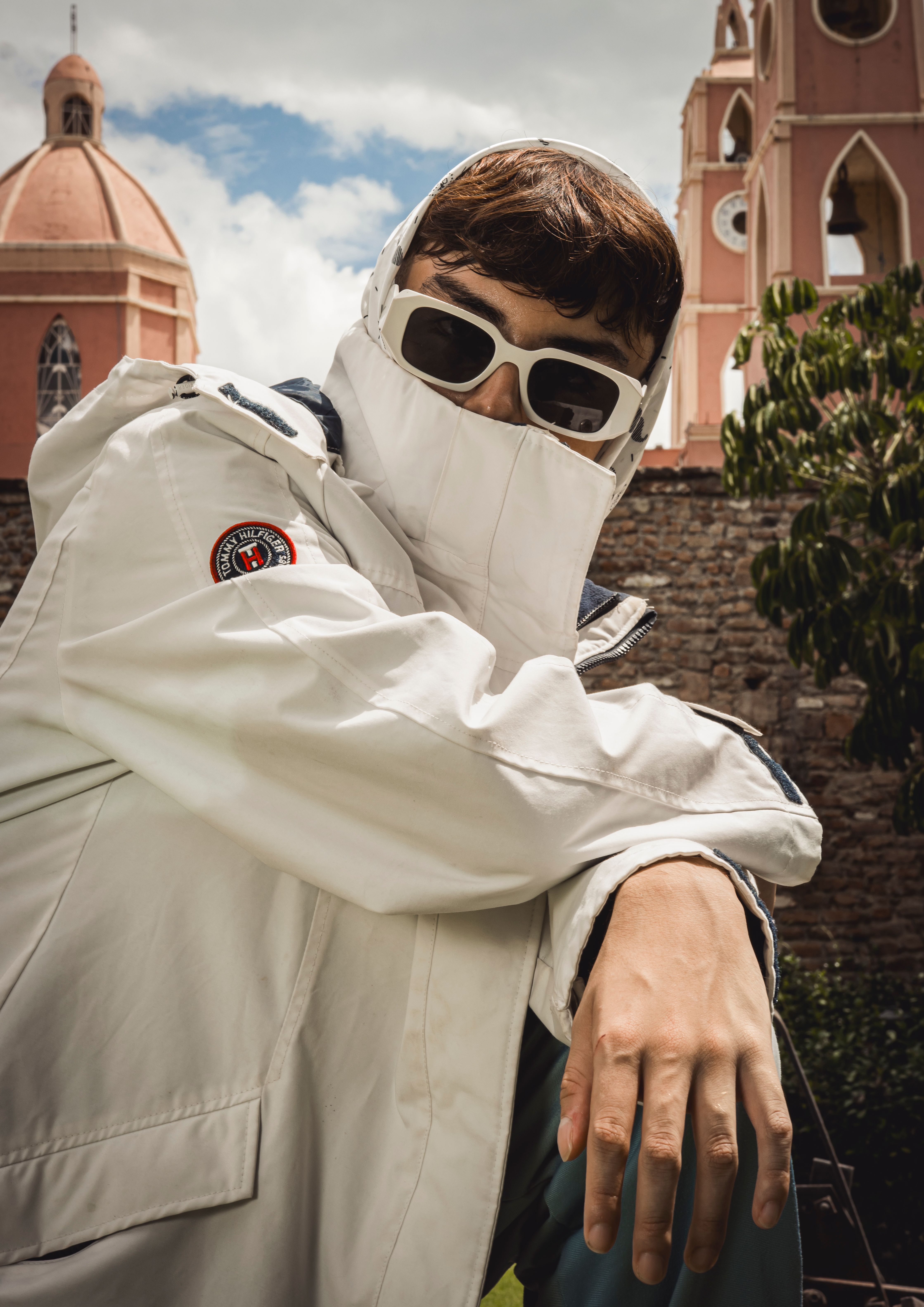 Stylish portrait of man in white jacket and sunglasses with historic towers backdrop