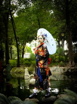 A geisha in a vibrant kimono with a parasol stands in a tranquil Japanese garden.