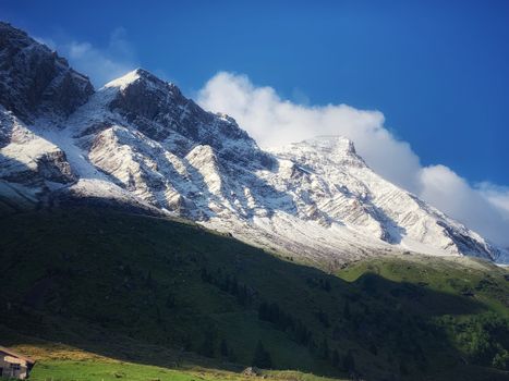 Breathtaking view of a snow-capped mountain with lush green valley under a bright blue sky.