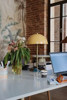 Stylish workspace featuring a laptop, lamp, and floral decor in a brick interior.