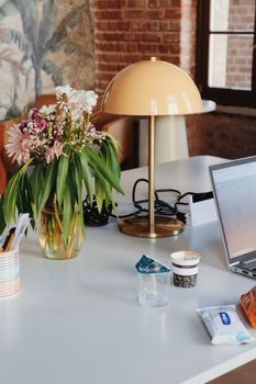 A modern workspace featuring a floral arrangement, laptop, and warm lighting for a cozy and productive atmosphere.