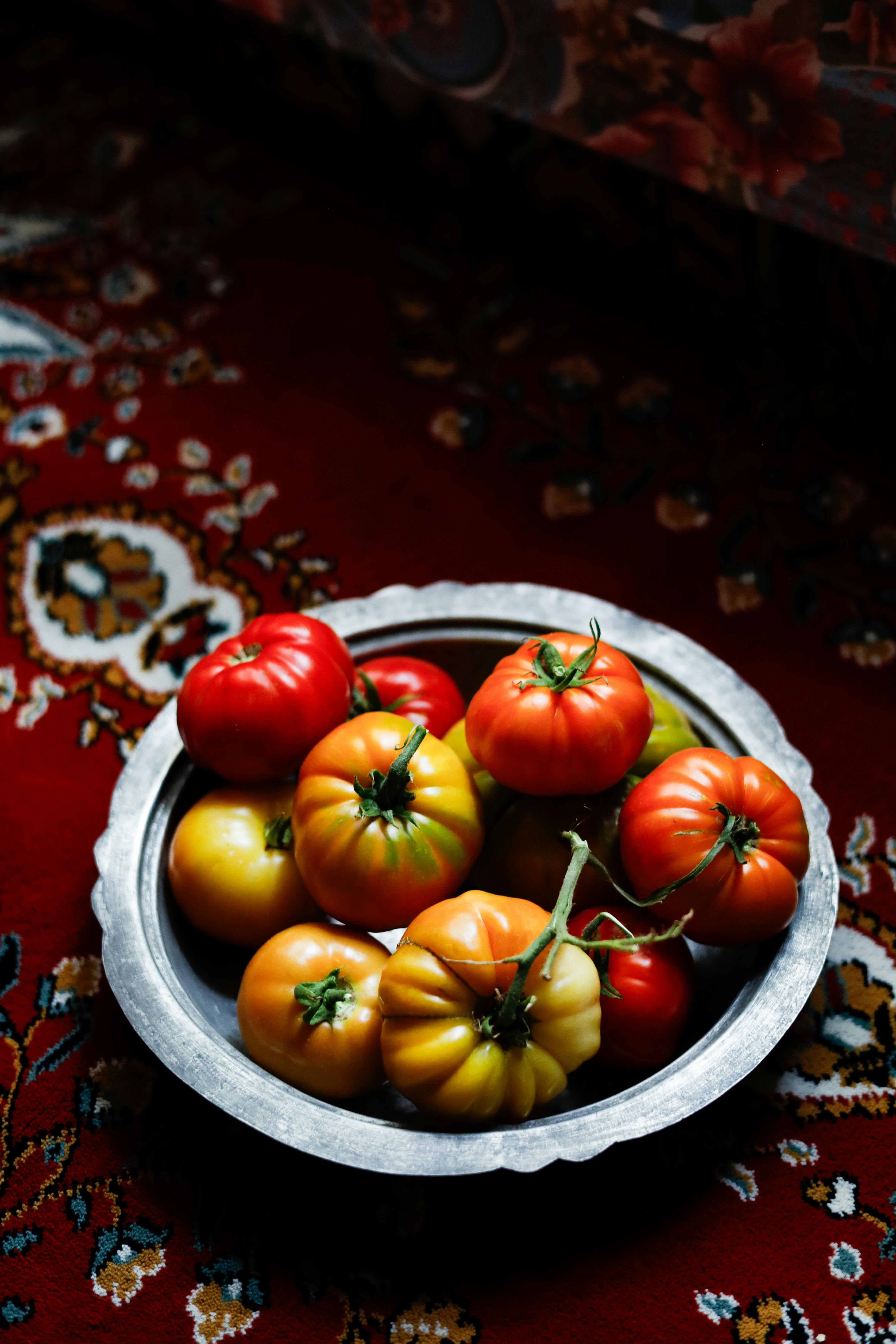 A bowl of colorful heirloom tomatoes on a decorative red background, perfect for fall themed projects.