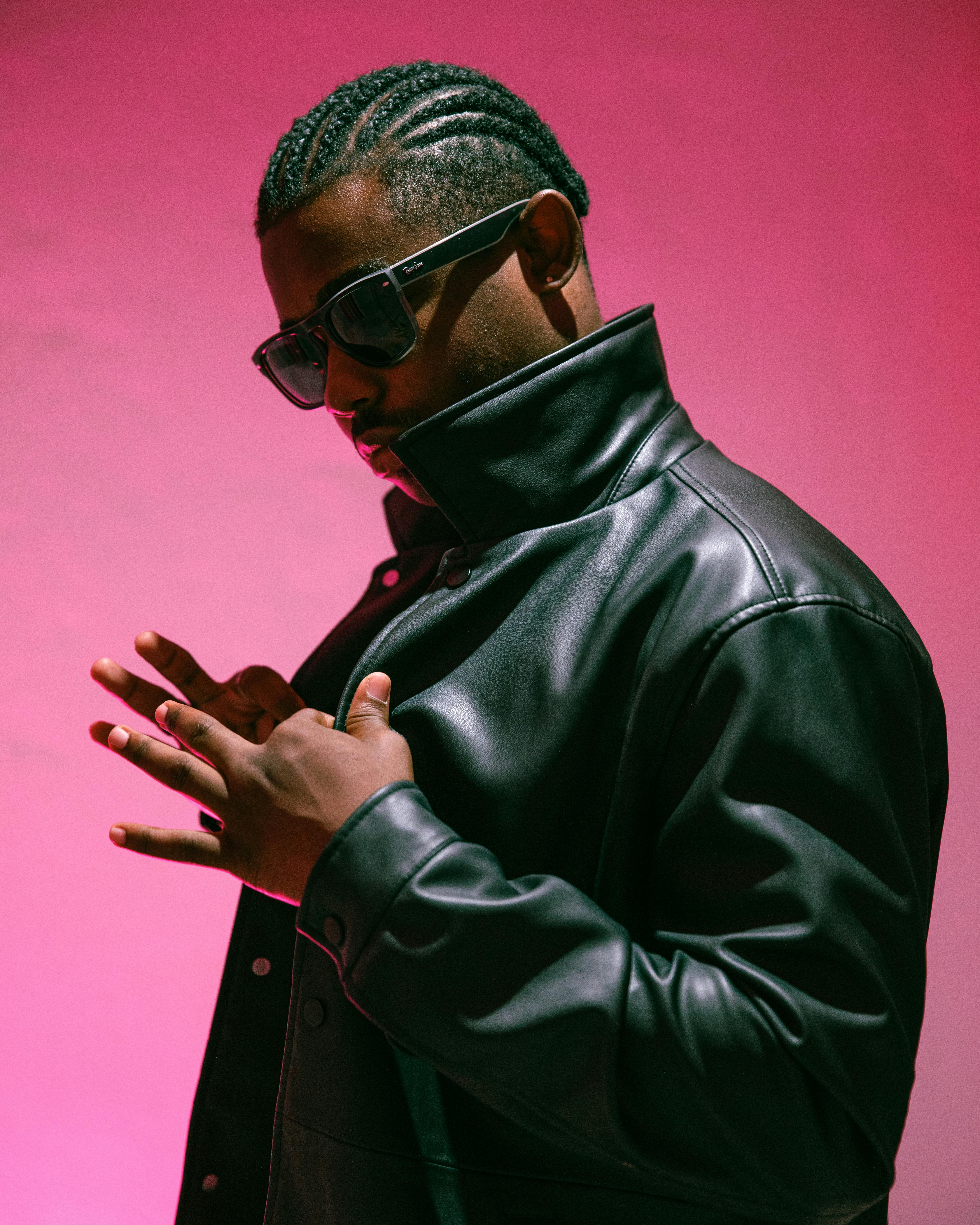 Portrait of a man in sunglasses and black leather jacket against a pink background.