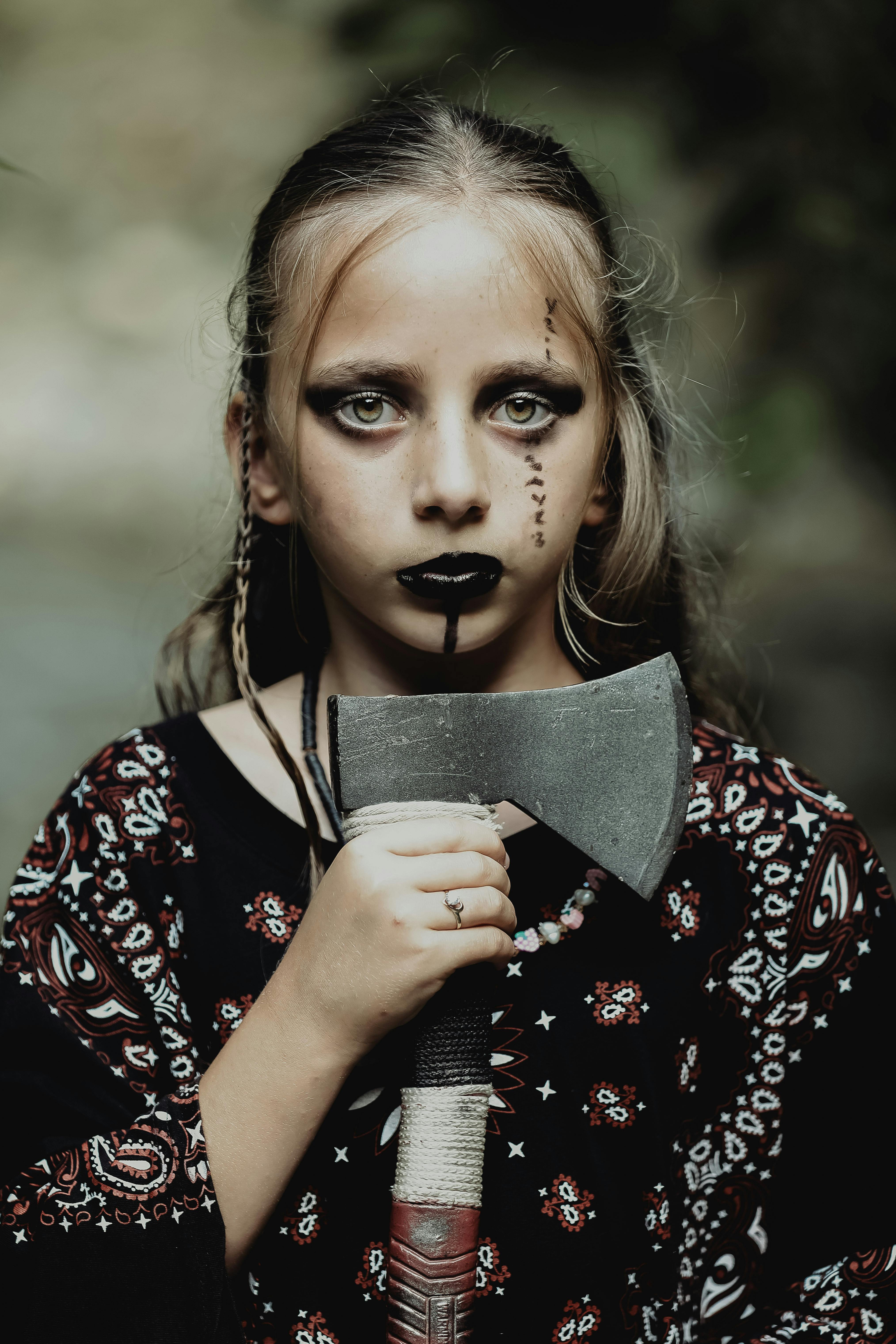 Close-up portrait of a young girl in a scary Halloween costume holding an axe.