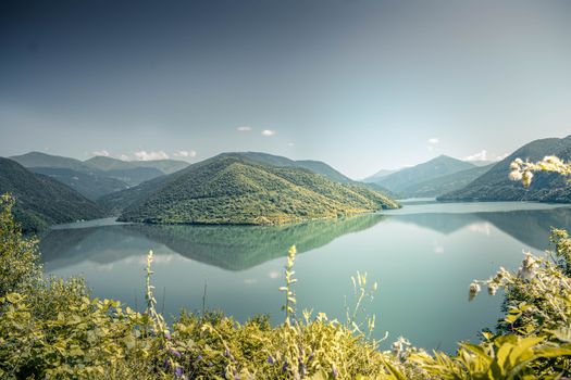 夏日晴朗的天空下，宁静的湖被郁郁葱葱的青山环绕