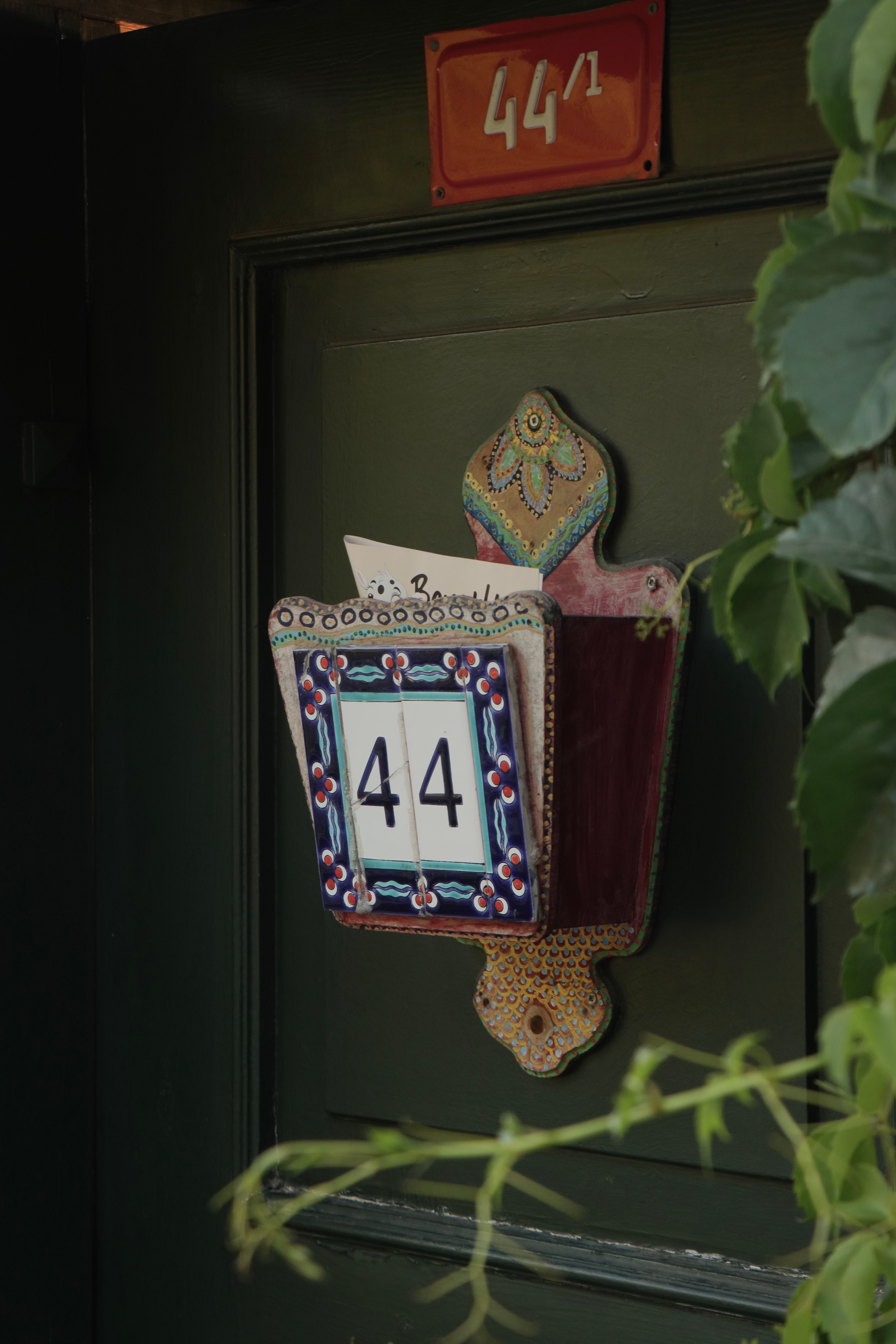 Colorful ceramic house number plate reads 44 on a vintage green door.