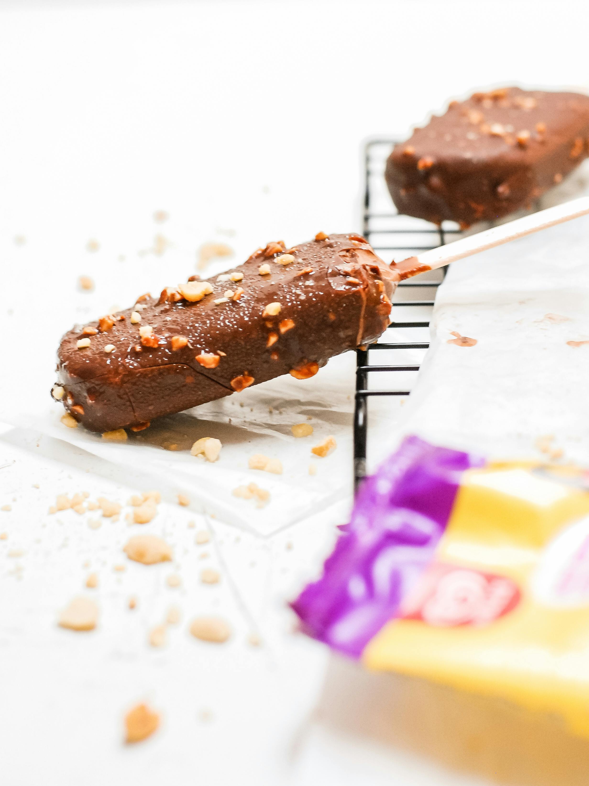 Close-up of chocolate ice cream bars with nuts on a cooling rack.