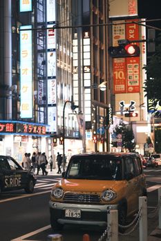 Lively street in Tokyo at night with cars and illuminated billboards.