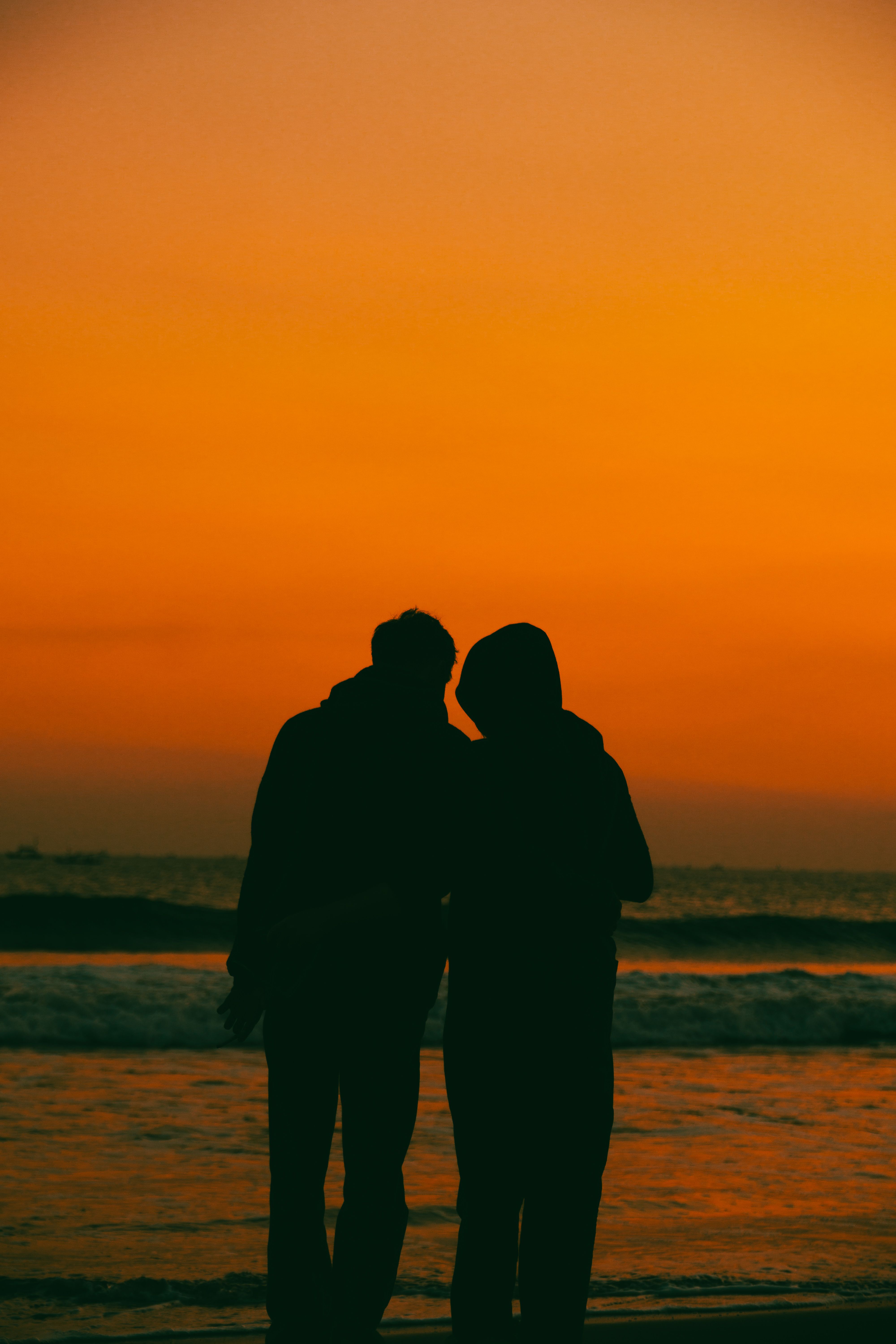 Two people are standing on the beach at sunset · Free Stock Photo