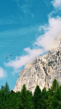 Scenic view of cable cars climbing the Dolomite Mountains in Cortina d'Ampezzo, Italy, on a sunny summer day.