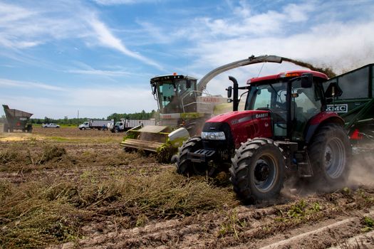 Active farming scene with red tractor and harvester in a rural field under blue skies.