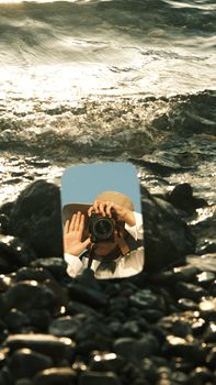 Photographer captures reflection in a mirror at the rocky seashore, conveying a creative summer vibe.
