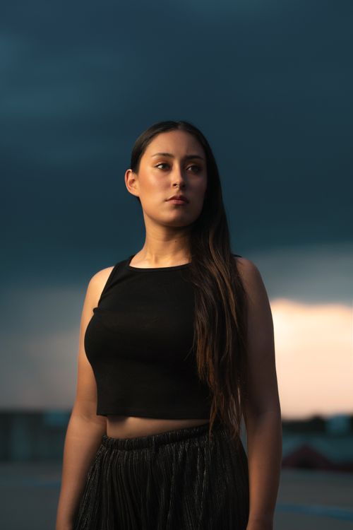 Free A strong, confident woman posing outdoors under a dramatic sky at sunset. Stock Photo