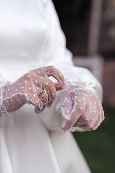 Close-up of a bride's hands wearing vintage lace gloves and wedding ring.