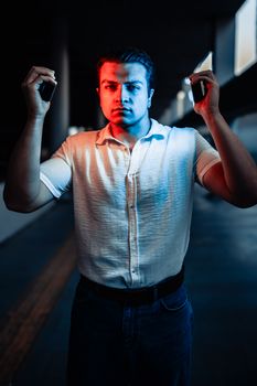 A man in a white shirt poses dramatically with mixed lighting effects indoors.