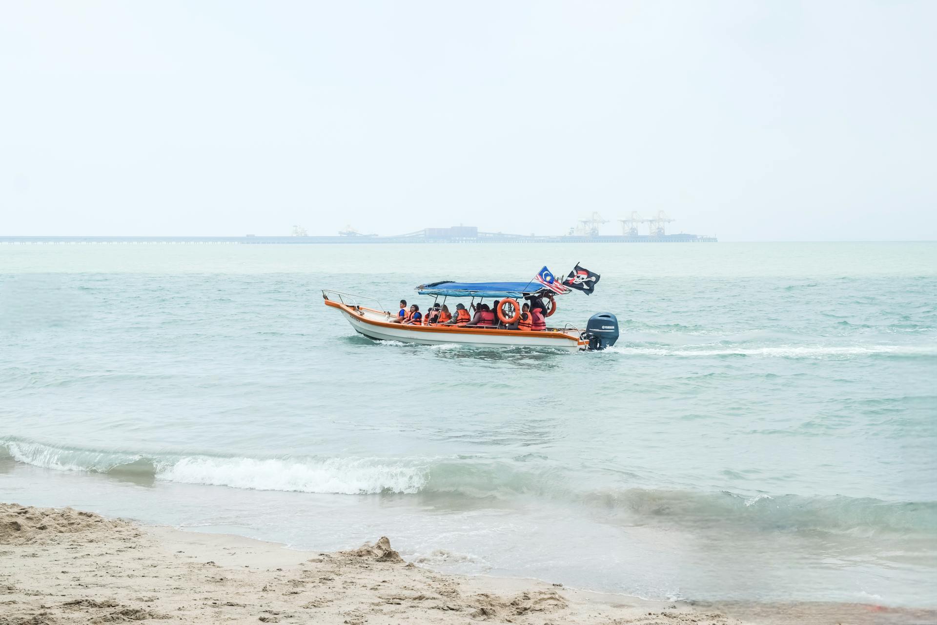 Tourists enjoy a boat ride on a calm beach in Lumut, Malaysia, under a bright sky.
