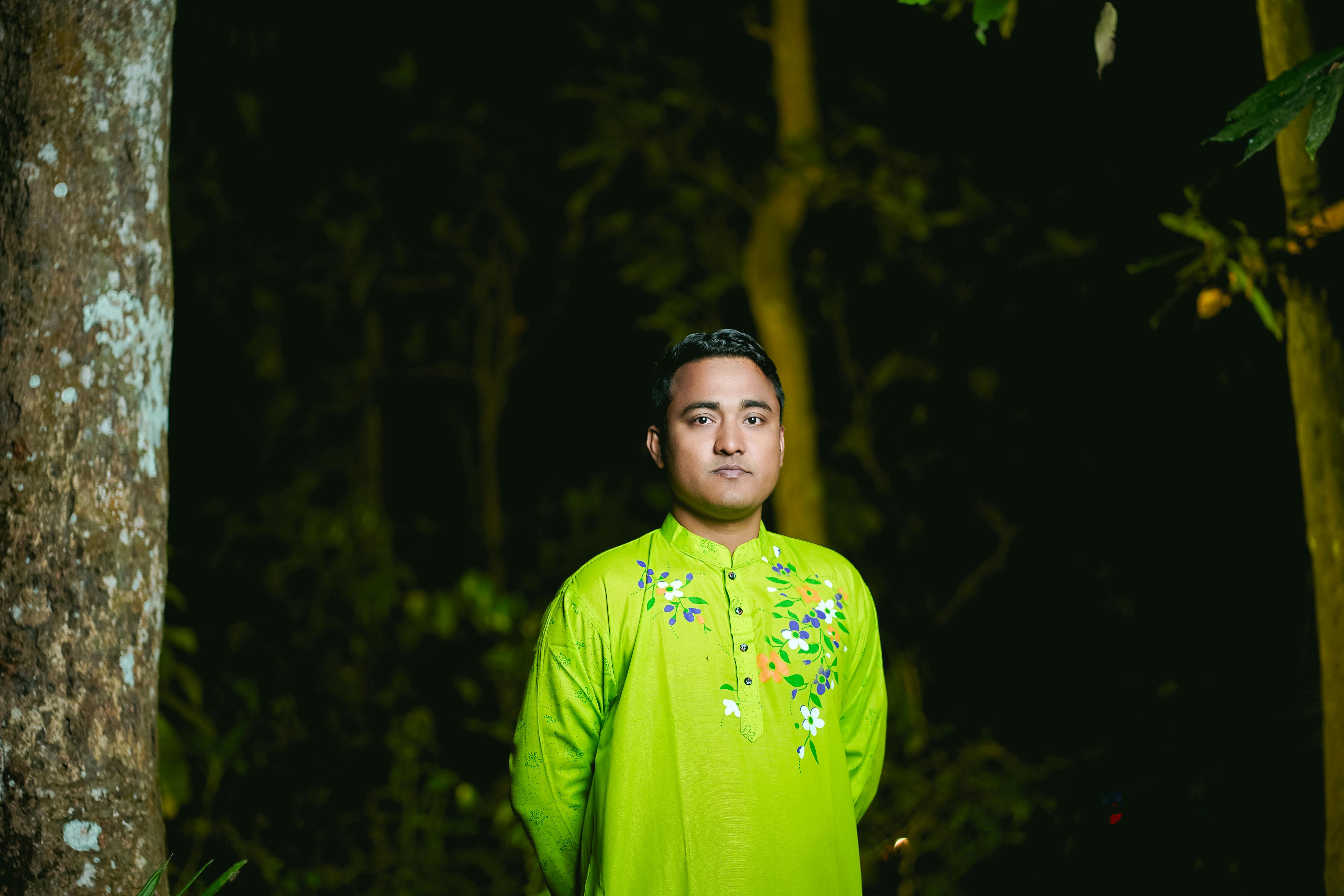 A man poses in vibrant green traditional attire amidst a lush outdoor setting.