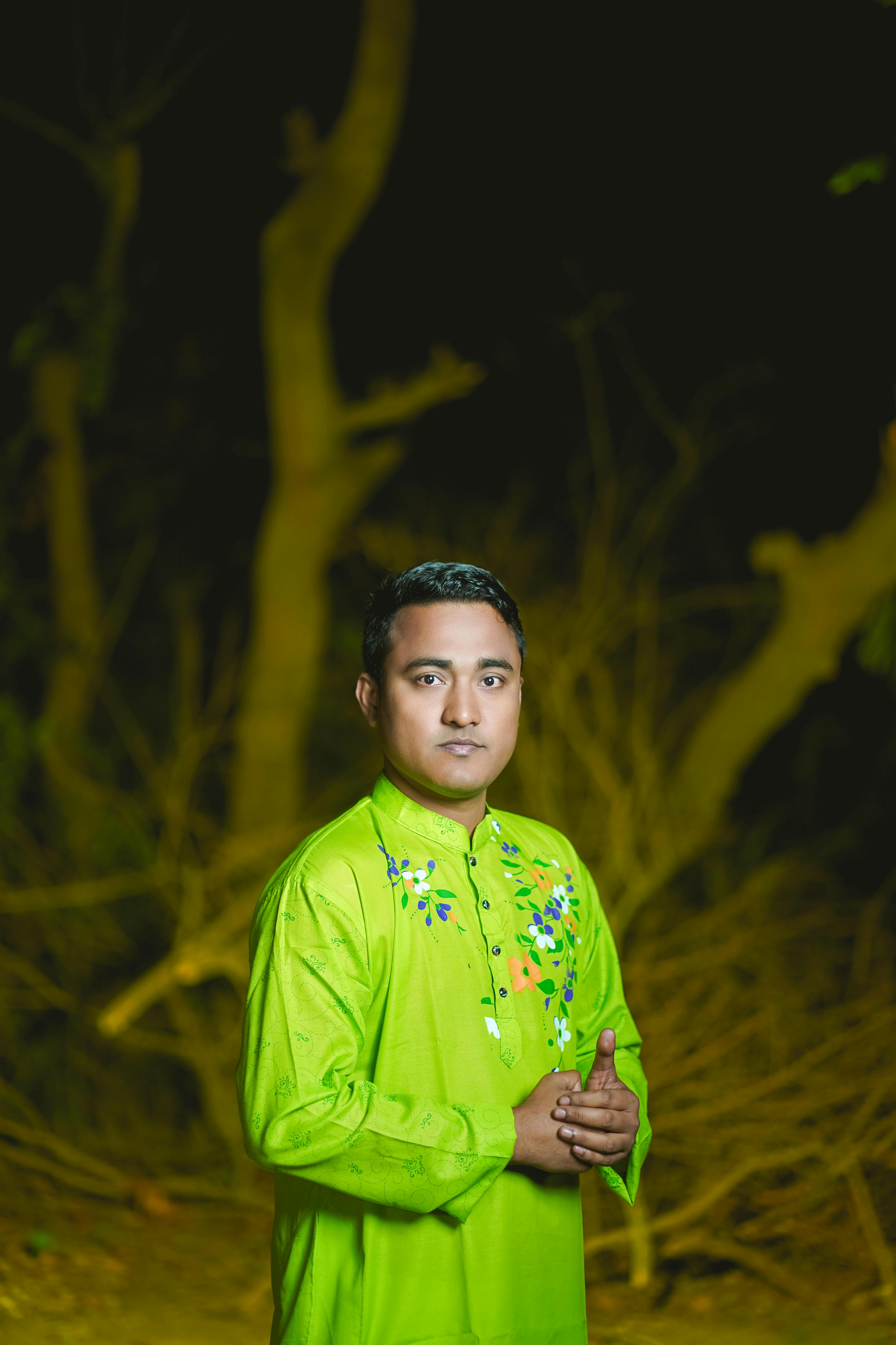 South Asian man in vibrant green traditional clothing poses confidently outdoors at night.