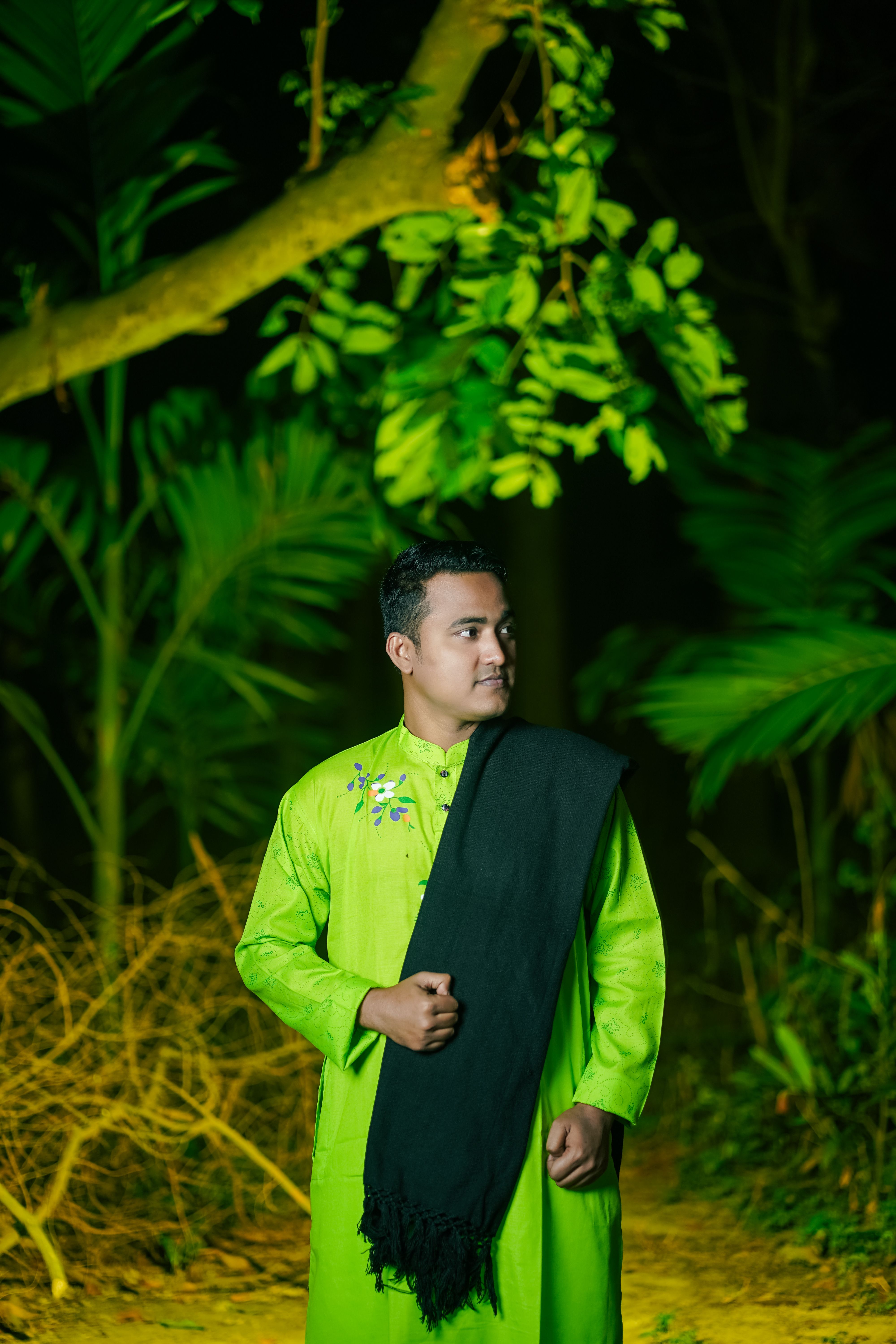 Portrait of a man in traditional attire amidst lush greenery, captured outdoors during the day.