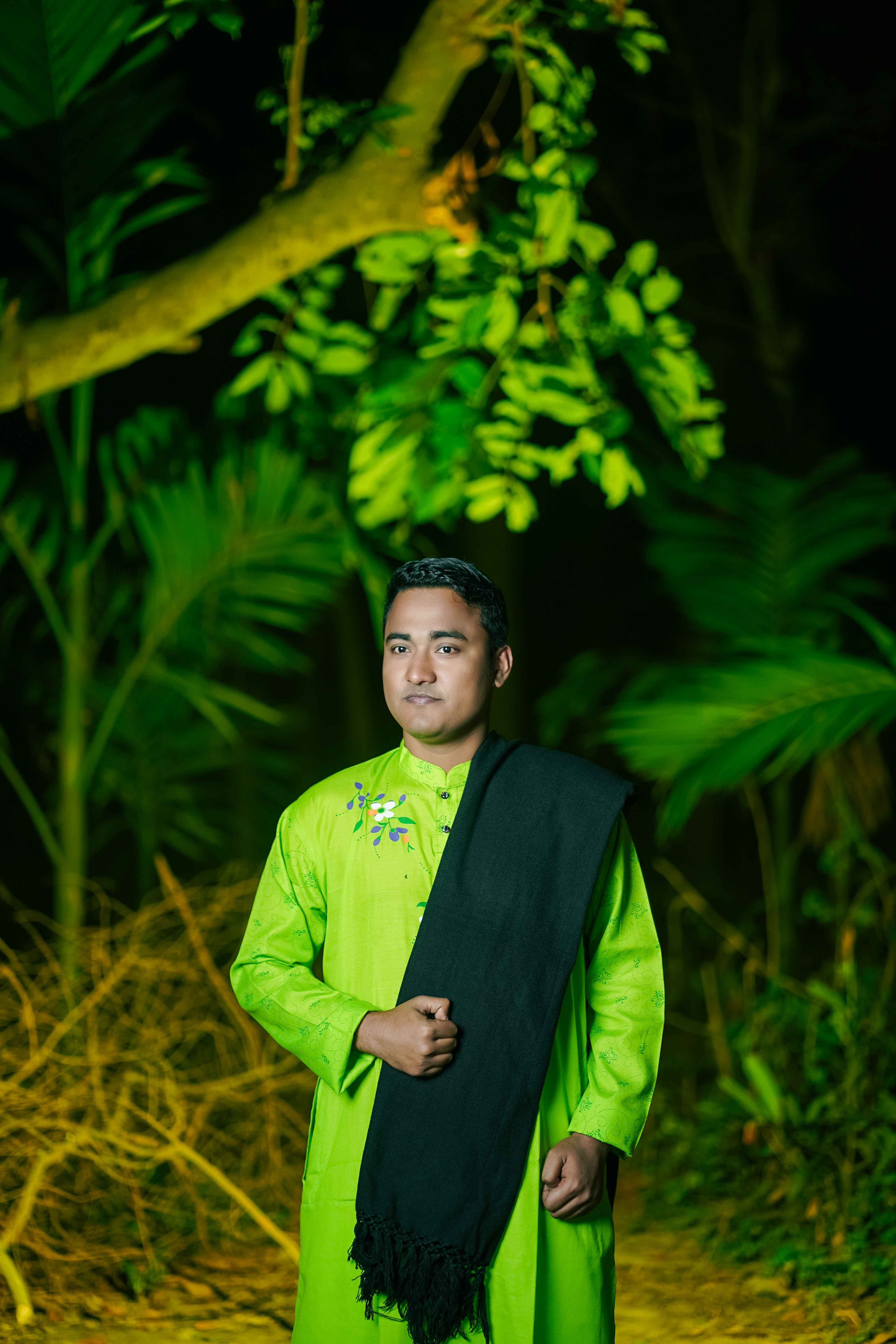 Man in vibrant traditional attire poses in lush greenery, Cumilla, Bangladesh.