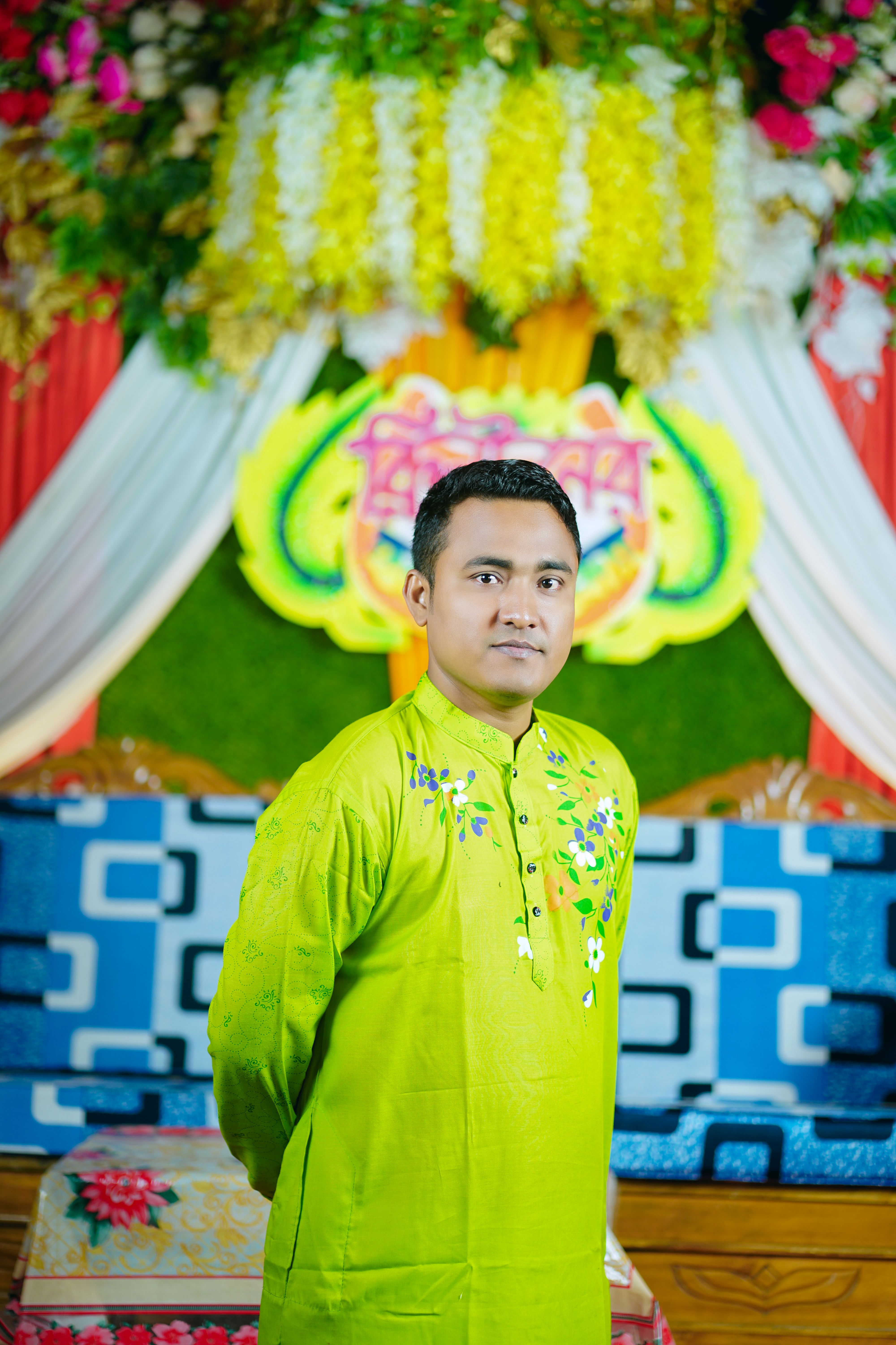 Man in traditional green attire at a vibrant Bangladeshi celebration indoors.