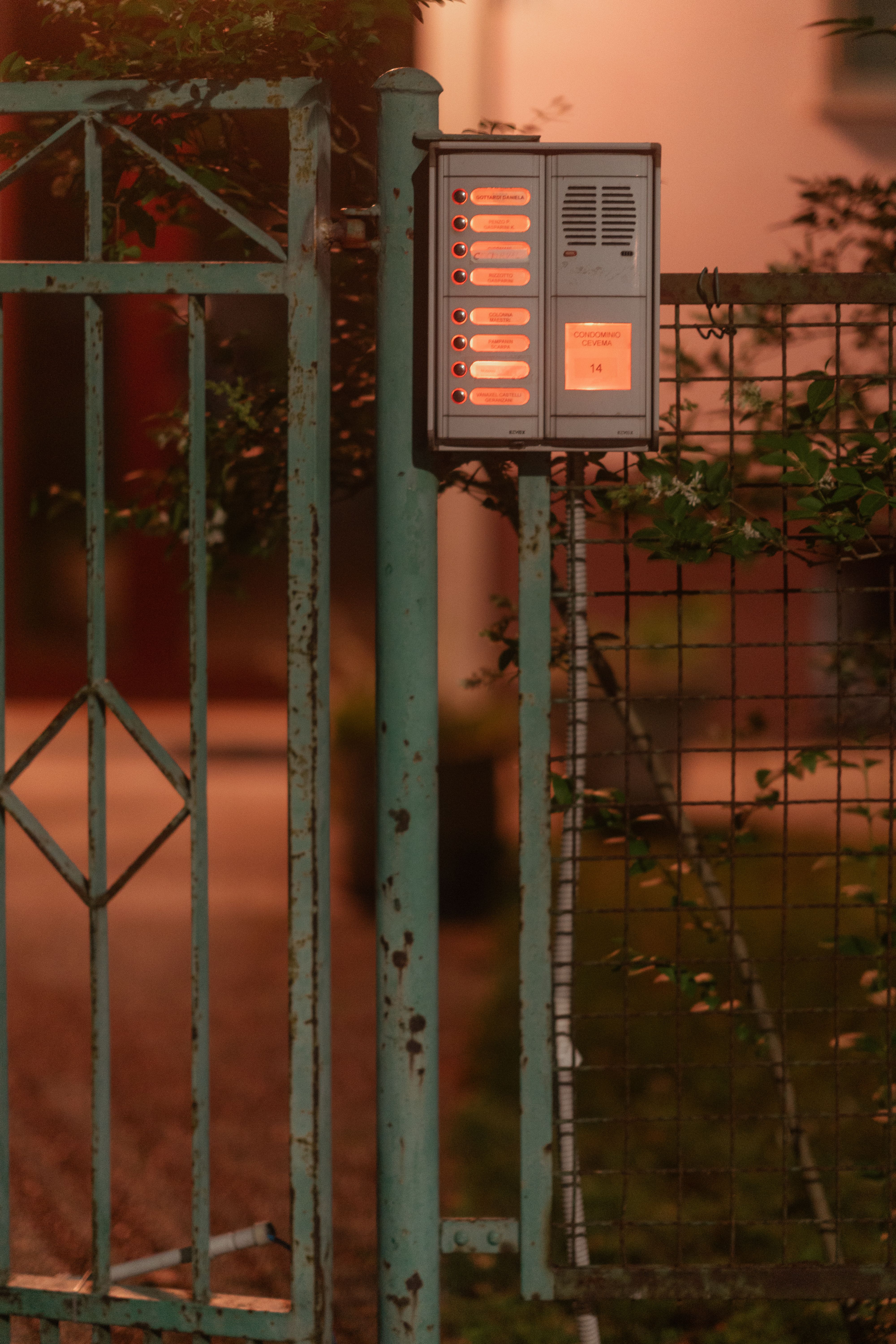 Rustic intercom system mounted on a weathered garden gate during nighttime in Italy.
