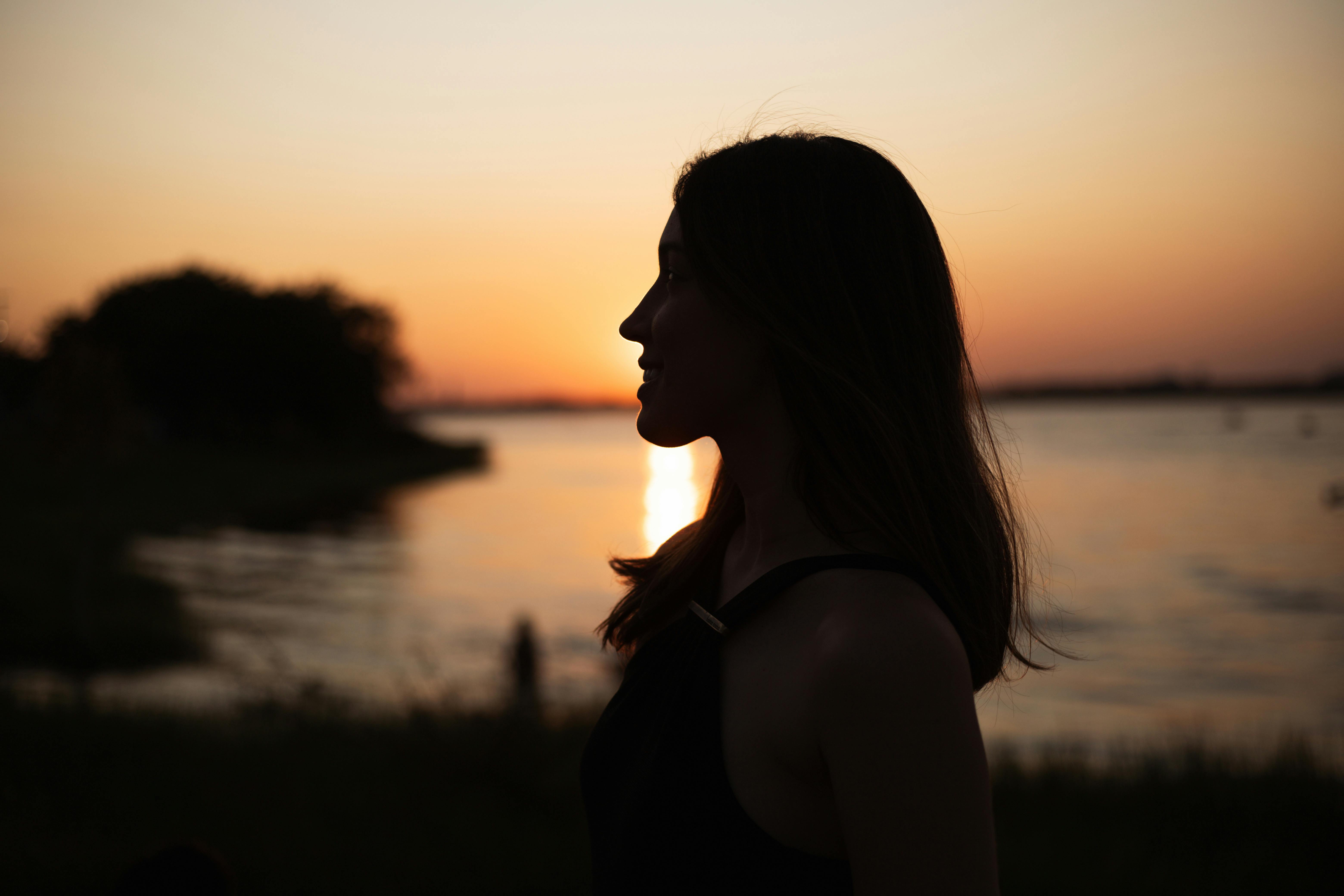 a woman standing by the water at sunset