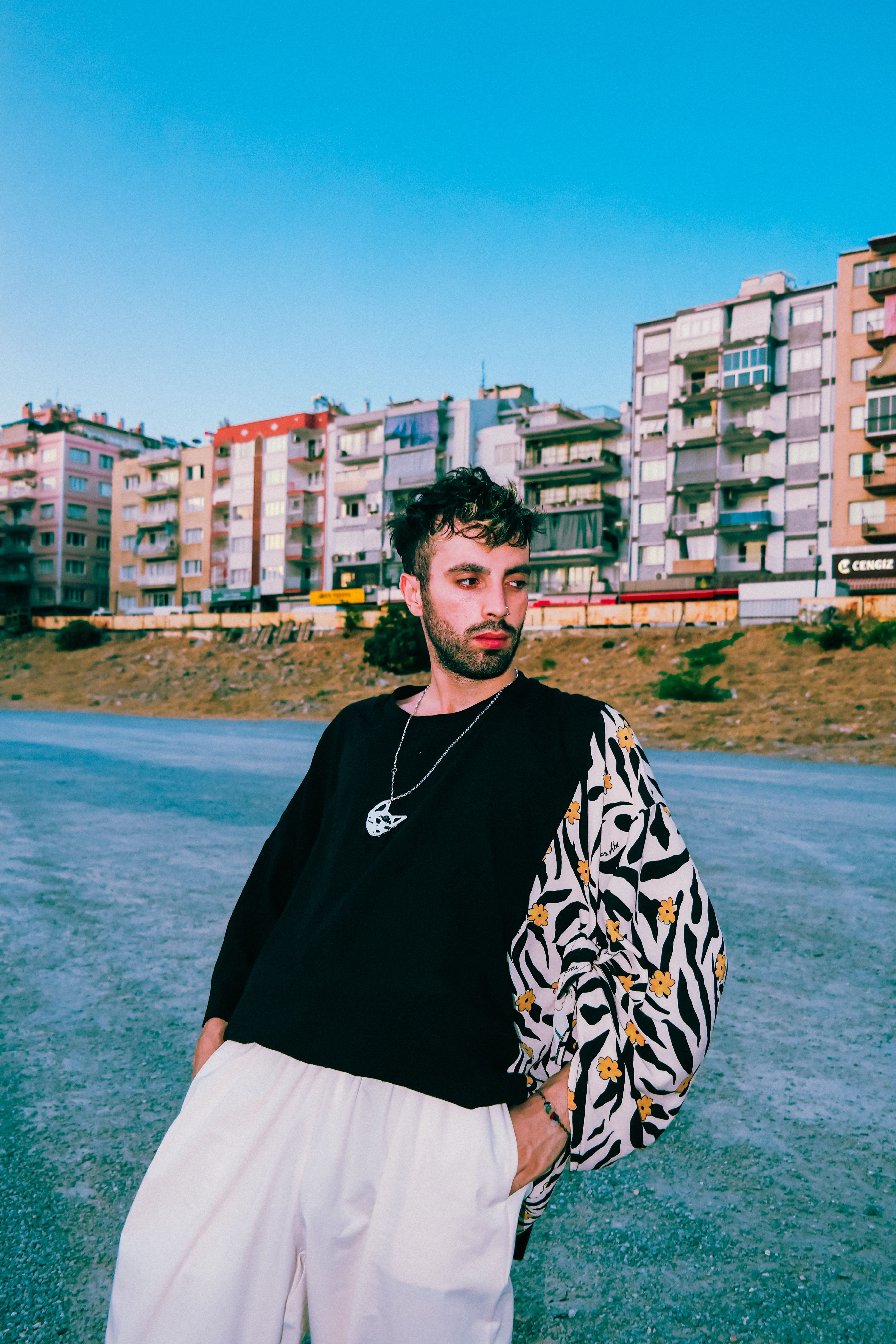 Fashionable man in vibrant urban setting with apartment blocks at dusk.