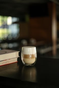 A stylish glass of cappuccino on a wooden table in a cozy indoor setting, perfect for coffee lovers.