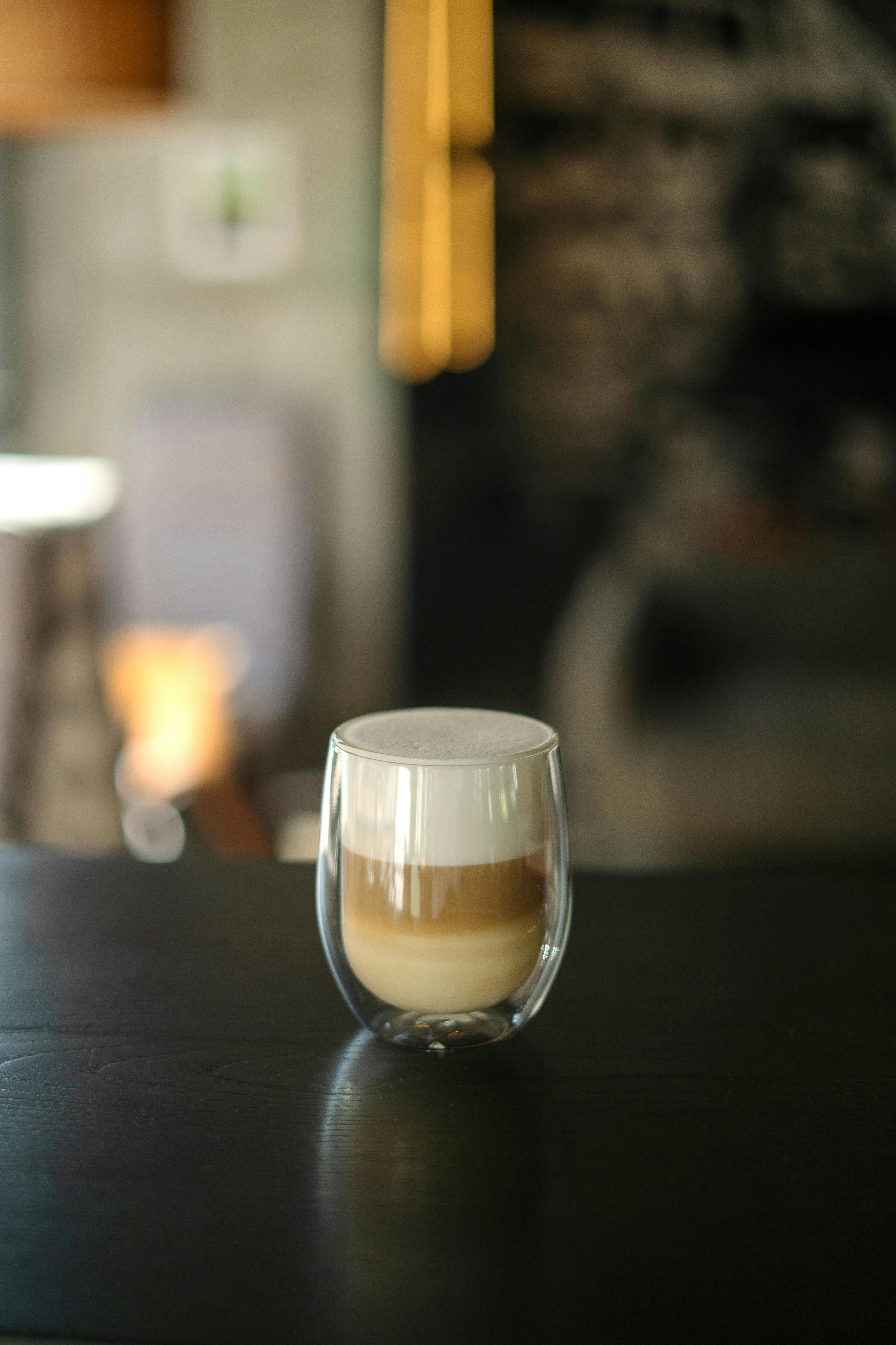 Stylish cappuccino in a double-walled glass on a dark wood table indoors.