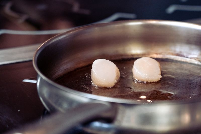 Close-up of scallops being seared in a stainless steel pan on a stovetop.