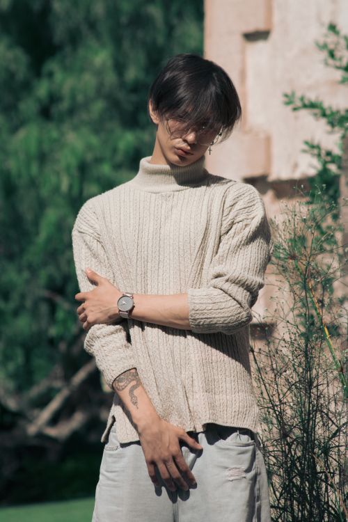 Free A fashionable young man poses in a cozy sweater against a natural outdoor background. Stock Photo