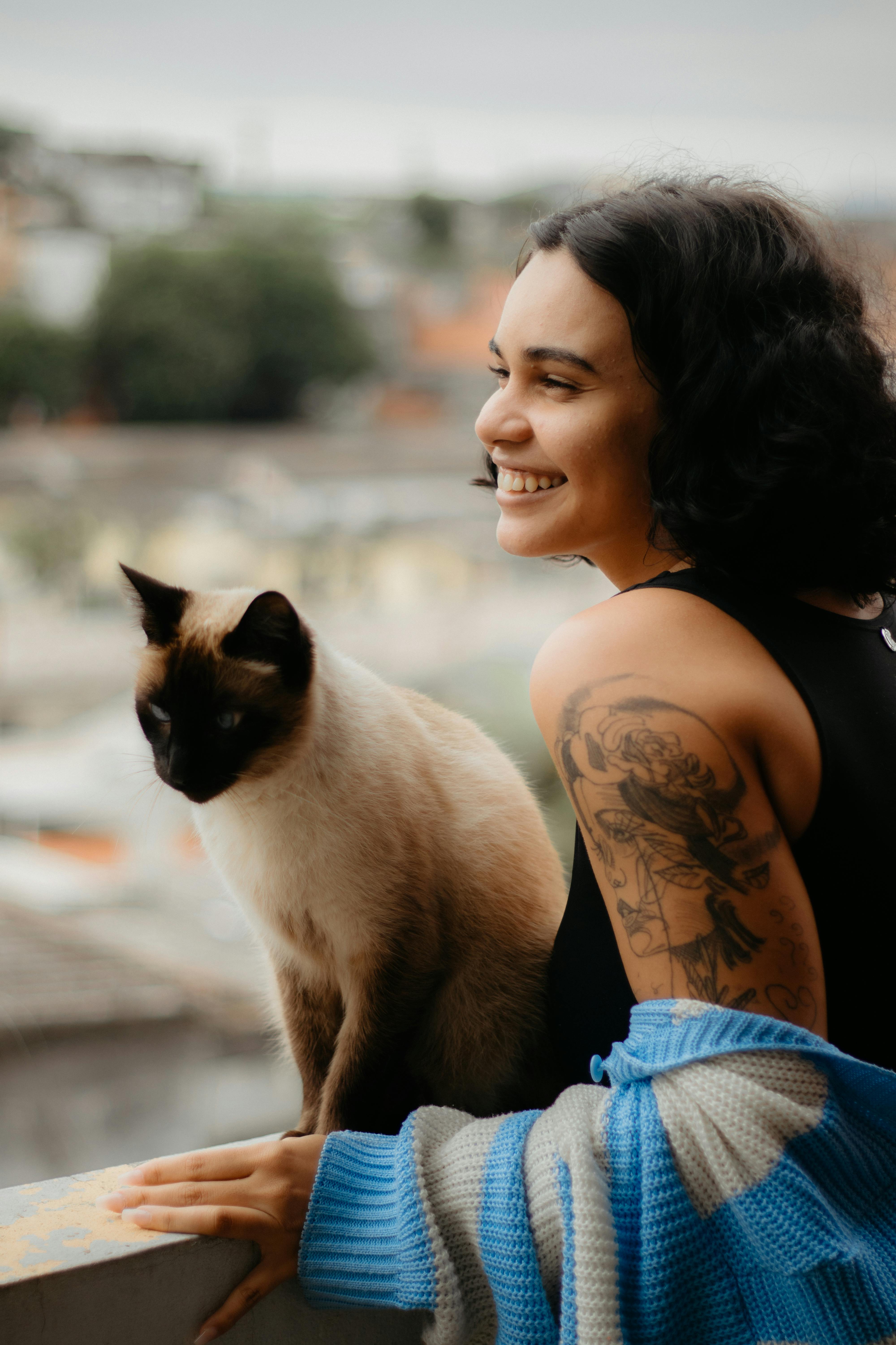 A woman with tattoos and a siamese cat on a balcony