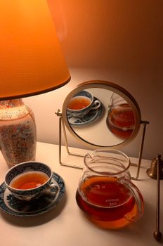 A teapot and teacup in a warm setting with ambient lighting and a mirror reflection.