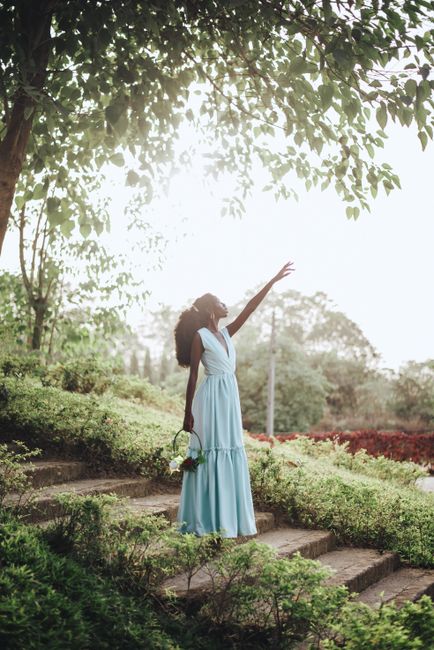 Elegant African woman in a blue dress reaching upward, standing on park steps in Abuja, Nigeria.