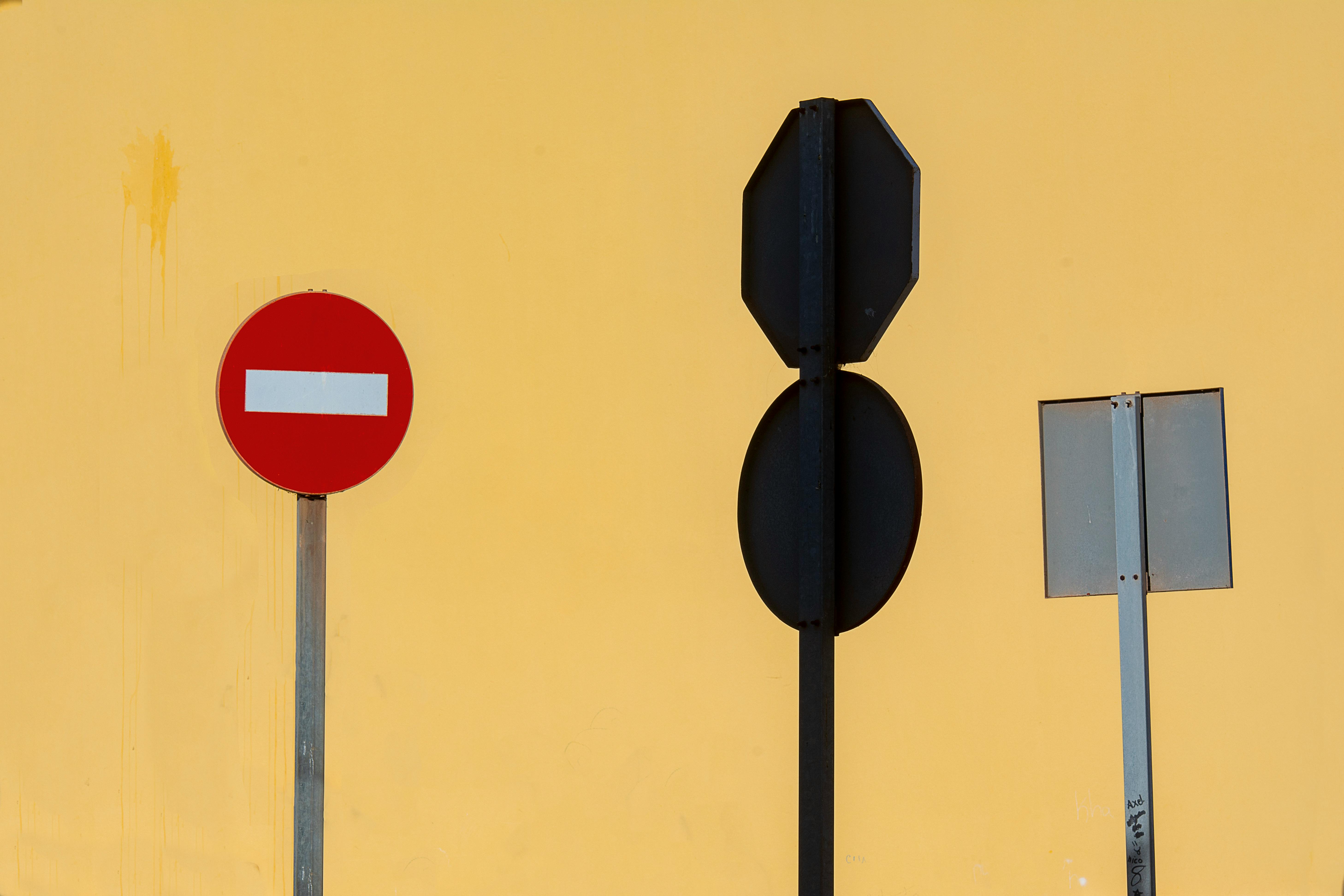 A collection of traffic signs in front of a bright yellow wall showcasing bold minimalism.