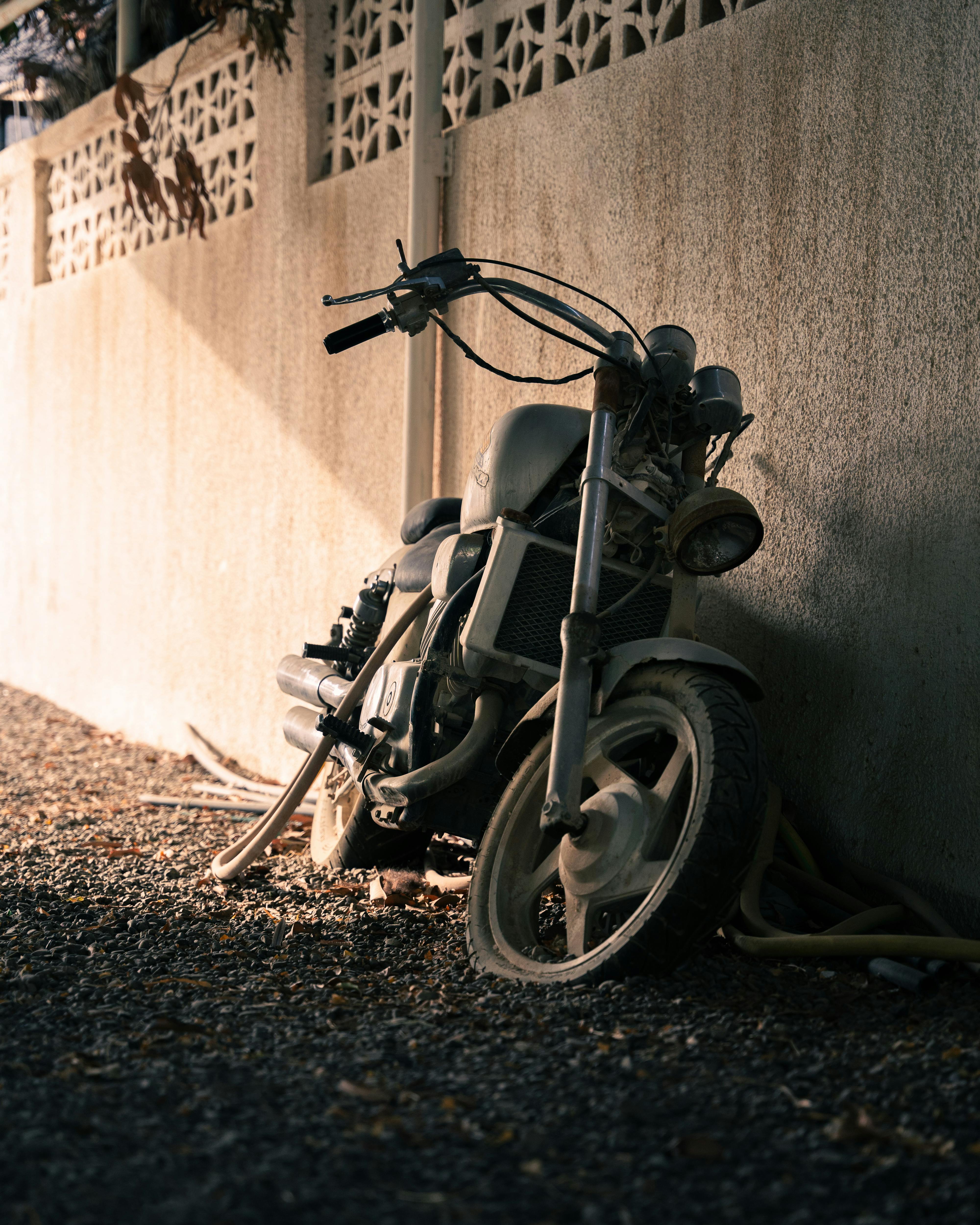 A vintage motorcycle rests against a sunlit wall, highlighting its rustic charm and history.