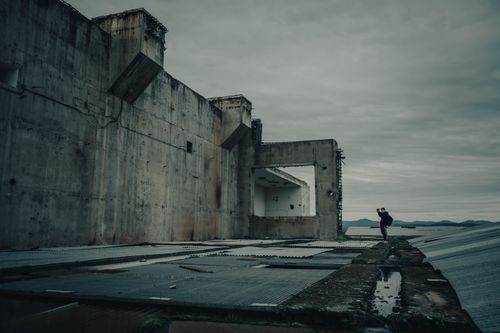 Free A solitary explorer stands beside an abandoned, decaying concrete structure. Stock Photo