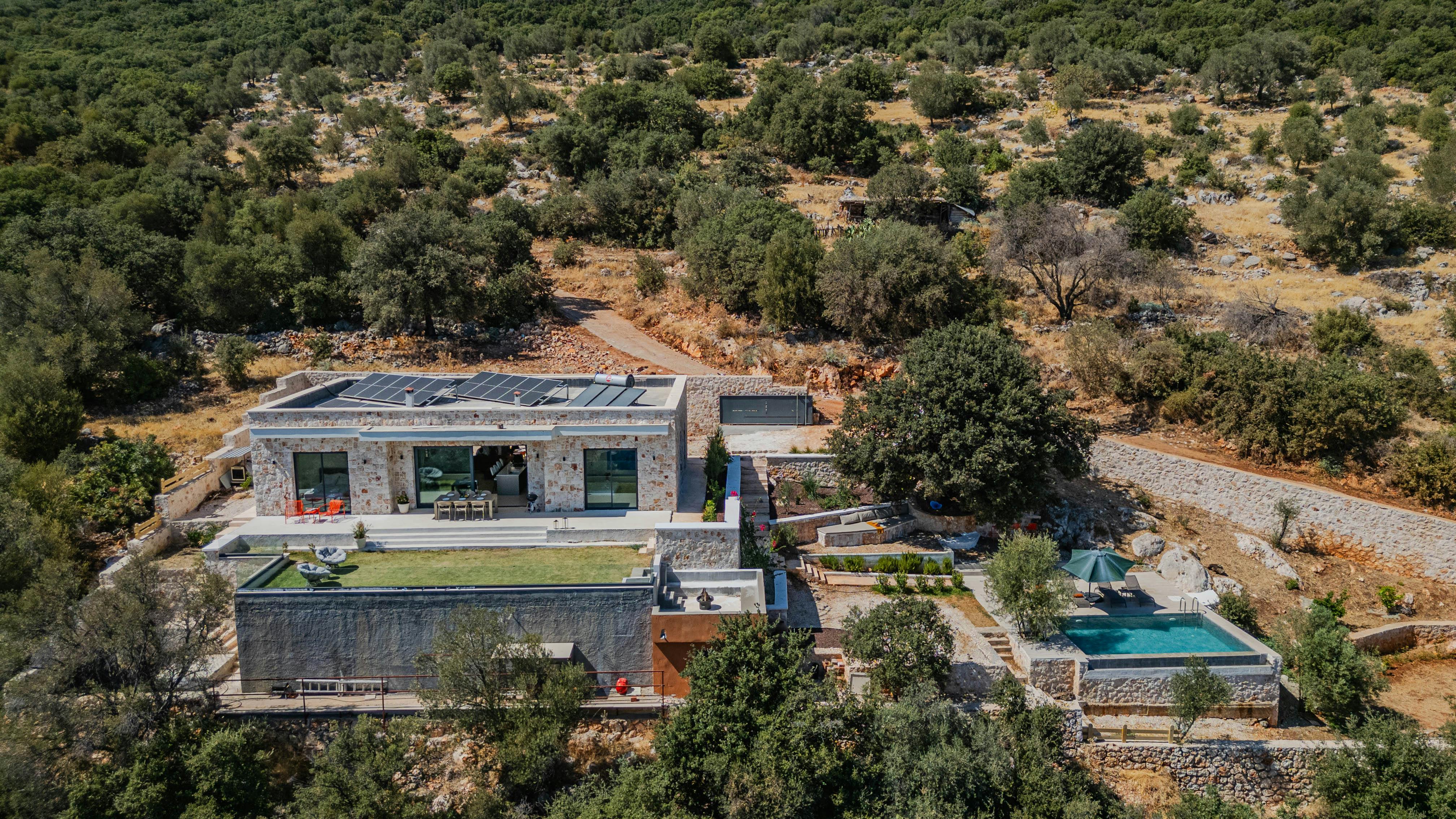 Aerial view of a modern luxury villa with a pool set in a scenic countryside landscape.