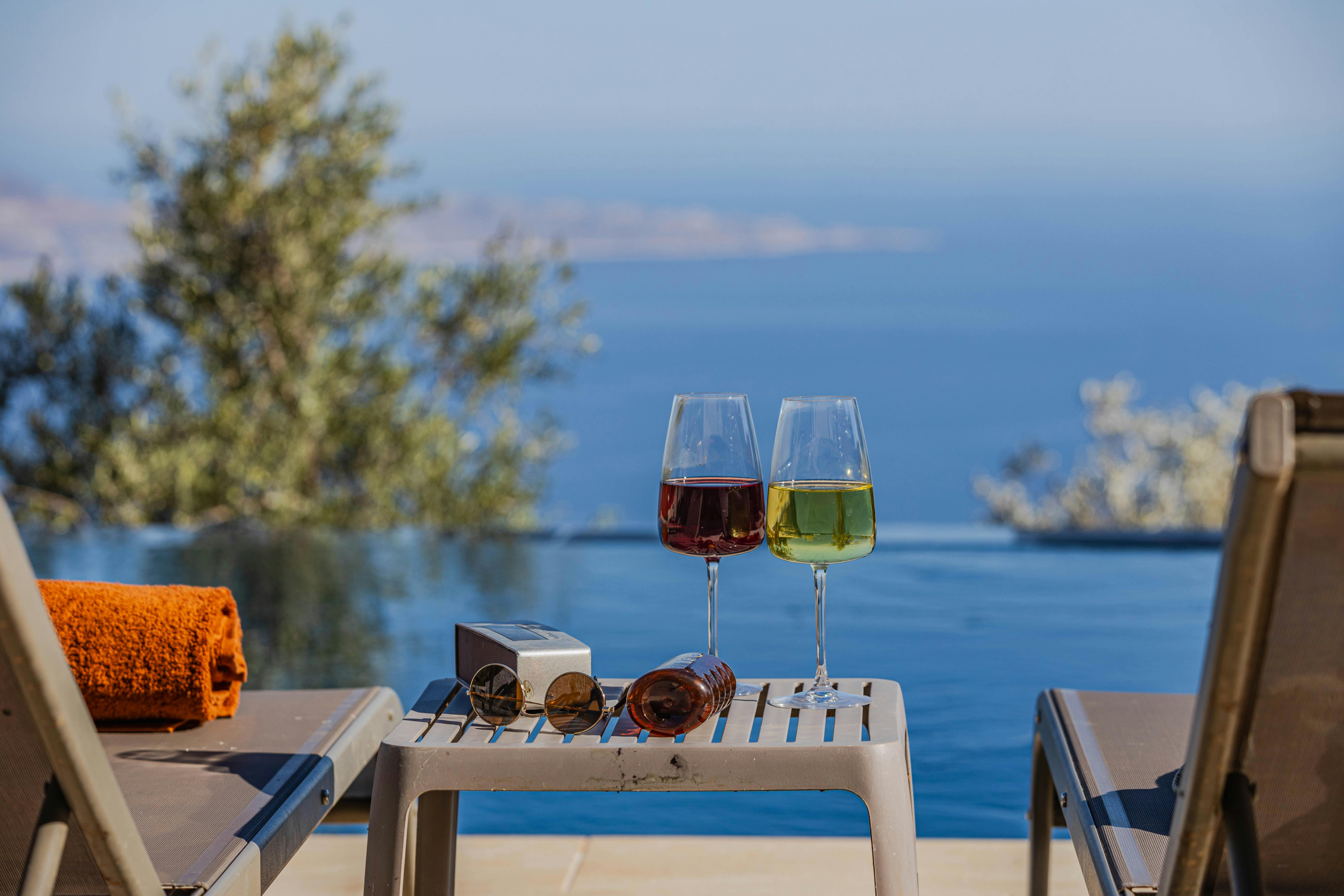 Enjoy a tranquil moment by the pool with wine and serene ocean views. Perfect for a luxurious vacation. - Photo by Ahmet ÇÖTÜR on Pexels
