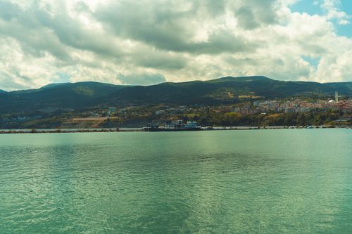 Free Panoramic view of a coastal city with lush mountains and serene water, under a cloudy sky. Stock Photo