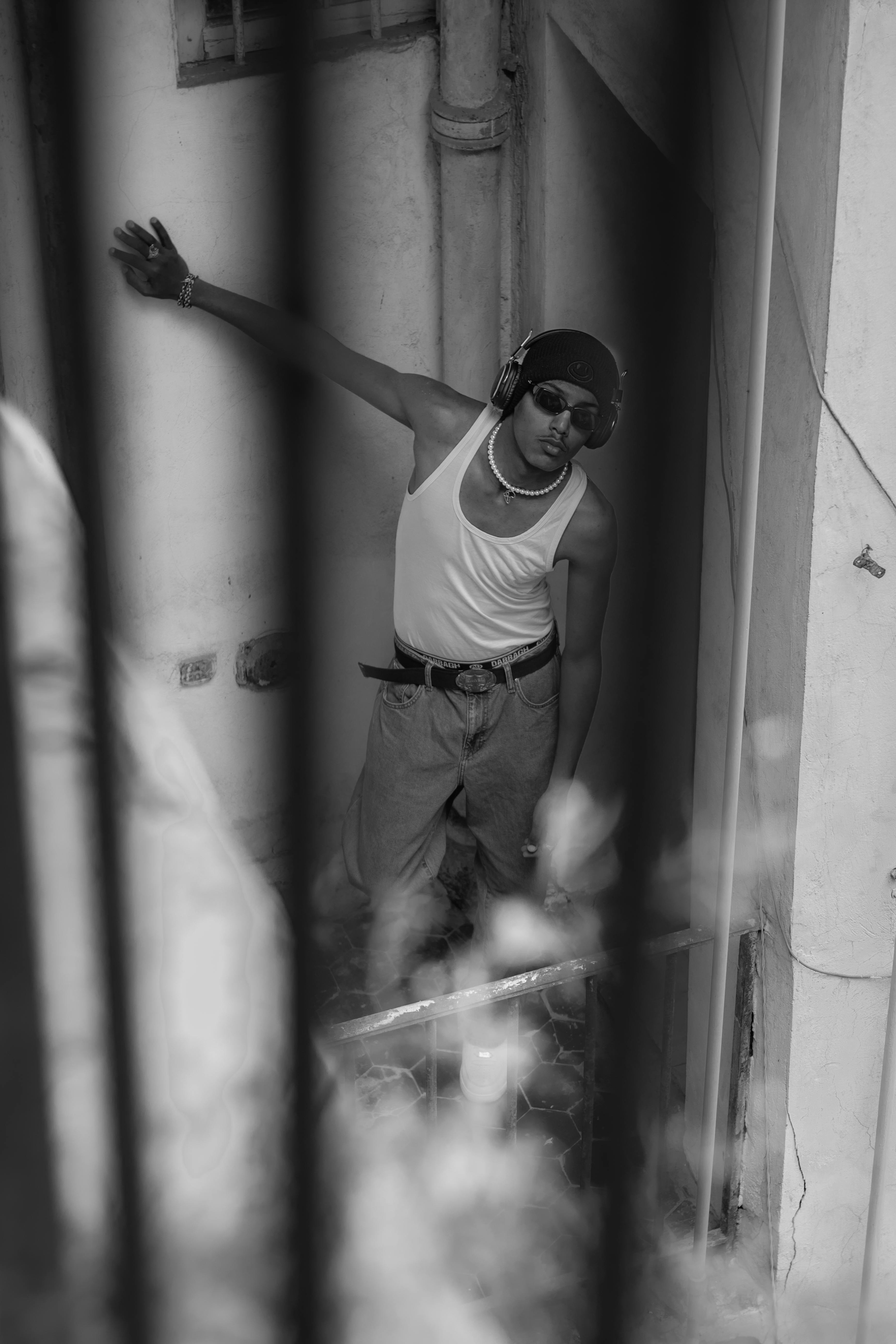 Black and white portrait of a young man in urban setting with headphones and sunglasses.