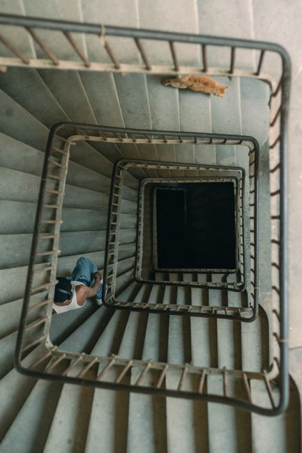 Top-down view of spiral staircase with a person descending, conveying urban exploration.