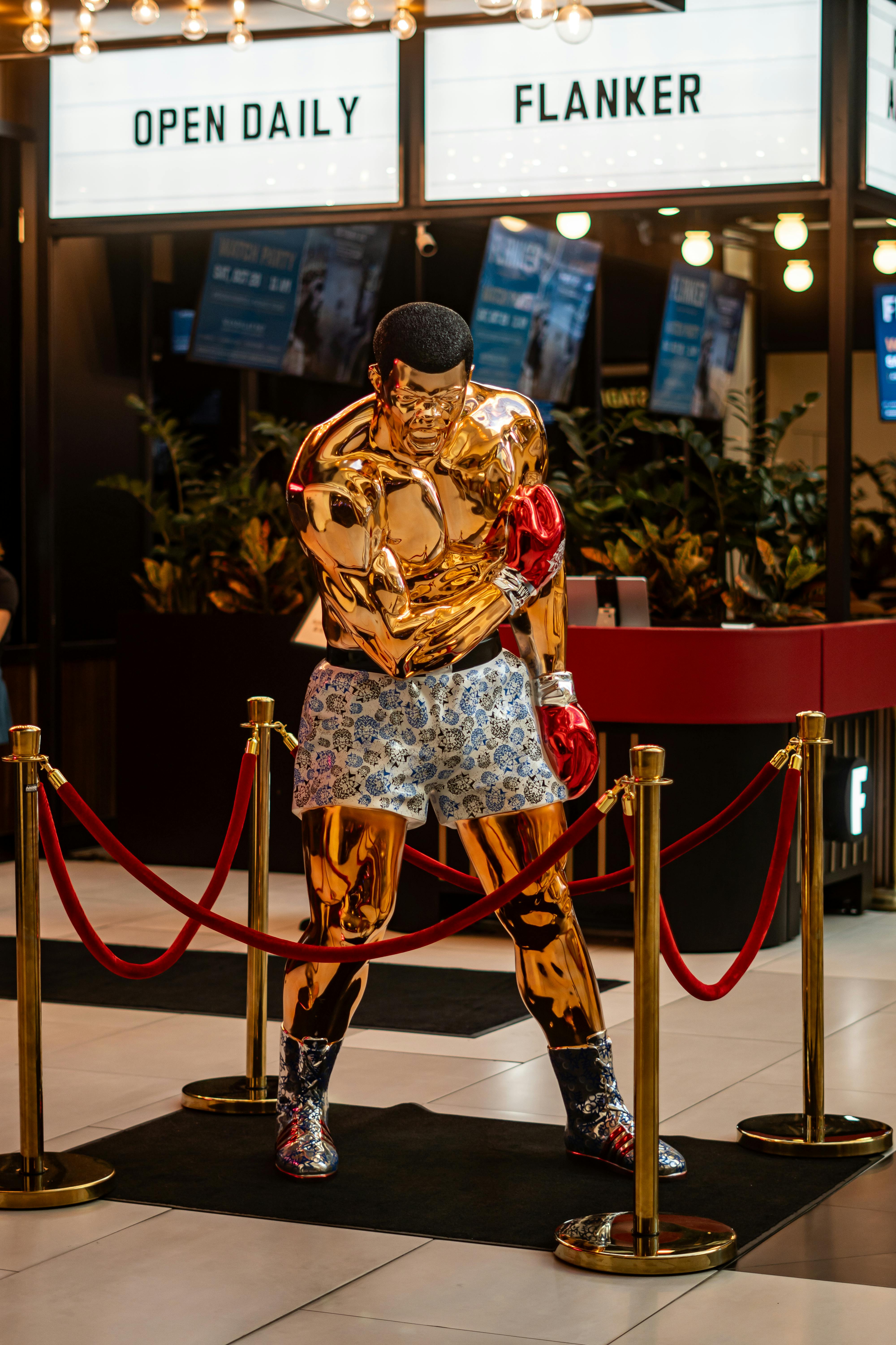 A striking golden boxer statue on display in a Las Vegas mall, elegantly roped off with vibrant decor.