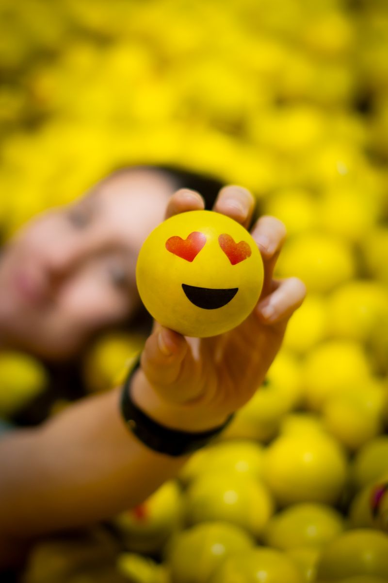 Hand holding a heart-eyes emoji ball above a pile of yellow smileys — victor dubugras on Pexels