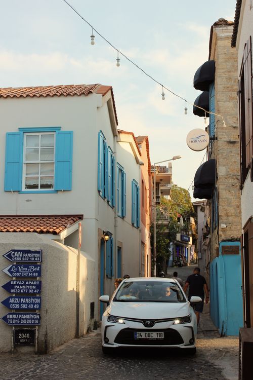 Free Charming narrow street with colorful shutters, a car, and people enjoying a sunny day. Stock Photo